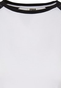 Hvid t-shirt med sort halsudskæring og raglanærmer. Lavet af blødt stof, har en glat tekstur og et minimalistisk design.