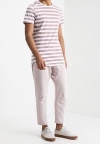 Camiseta a rayas en rosa claro y blanco, combinada con pantalones jogging rosa claro. Presenta un cuello redondo y un diseño ajustado, usada con zapatillas blancas.