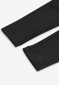 Leggings neri in cotone con una texture liscia, caratterizzati da bordi puliti e cuciture semplici. Il tessuto appare elasticizzato e confortevole.