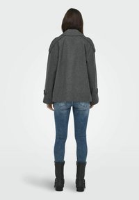 Veste en mélange de laine grise avec un col classique, coupe ample et grands accents de boutons, portée sur un jean en denim bleu et des bottines noires.