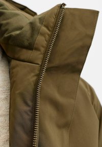 Olivgrüne Jacke mit Reißverschluss, die eine glatte Stoffstruktur aufweist. Der Kragen ist umgeschlagen und zeigt ein kontrastierendes Innenfutter.