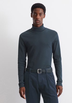Dark green turtleneck sweater made of smooth fabric, paired with textured navy corduroy pants and a black belt with a silver buckle.