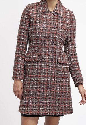 Femme portant un manteau en laine à carreaux marron et rouge, longueur genoux, croisé, avec un large col et des poches à rabat.