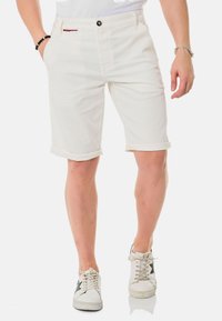 Shorts en denim blanc avec ourlets roulés, dotés d'une poche avant, d'une fermeture à bouton noir et d'une petite étiquette rouge sur la taille.