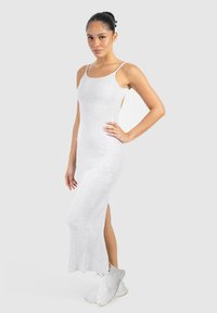 Robe maxi blanche sans manches avec un design ajusté, texture côtelée, fentes latérales et fines bretelles, associée à des baskets blanches.