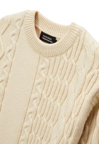 Pull beige tricoté avec un motif torsadé, doté d'un col rond côtelé et d'un tissu texturé, étiqueté "MONOPRIX" sur l'étiquette intérieure.