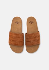 Sandali in suede marrone con una larga fascia superiore perforata e suole piatte. Soletta parzialmente imbottita con stampa del logo.