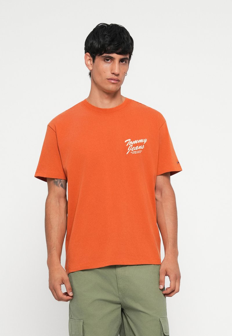 Orange cotton T-shirt with a round neckline and short sleeves. Features white “Tommy Jeans” logo on the left side and casual fit.