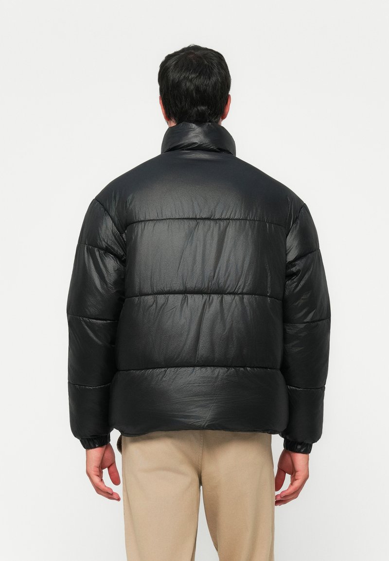 Czarna kurtka puchowa o błyszczącym wykończeniu, w oversize'owym fasonie, z poziomym pikowaniem i wysokim kołnierzem. Elastyczne mankiety i dół zapewniające pewne dopasowanie.