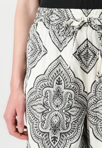 Pantaloni leggeri e stampati con vita elastica. Presentano un design geometrico in bianco e nero, tessuto morbido e un dettaglio in vita legato.