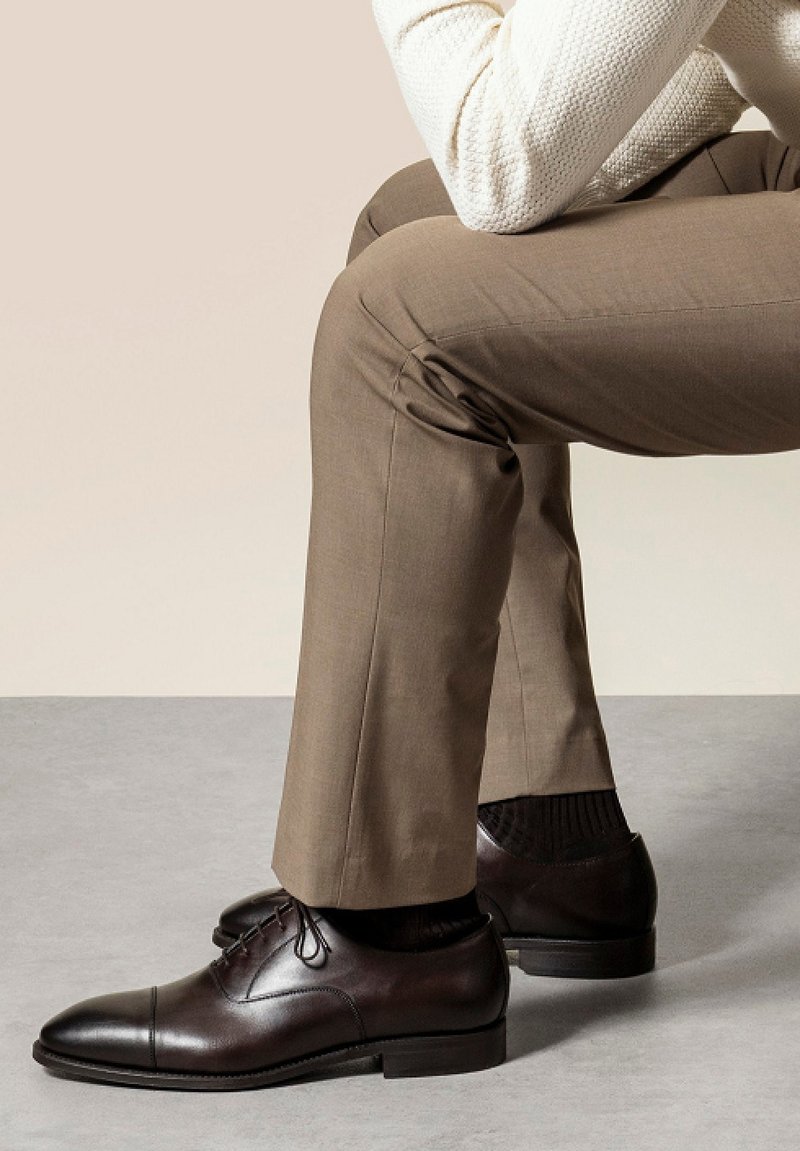 Bruine leren schoenen met een gladde afwerking, met een cap toe ontwerp en vetersluiting, gecombineerd met lichtbruin pantalon en een gestructureerde witte trui.