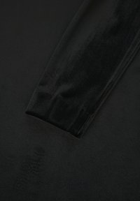 Tissu en velours noir exposé, présentant une texture douce avec une surface lisse. Le tissu est plié, montrant sa qualité dense et luxueuse.