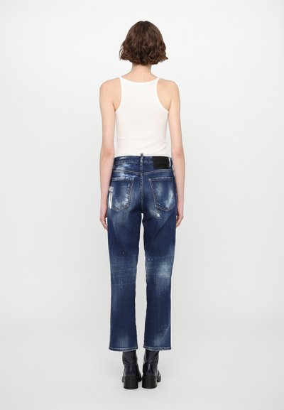 Jeans di denim con lavaggio medio, leggermente strappati, design a cinque tasche e vestibilità dritta, abbinati a un top bianco senza maniche.