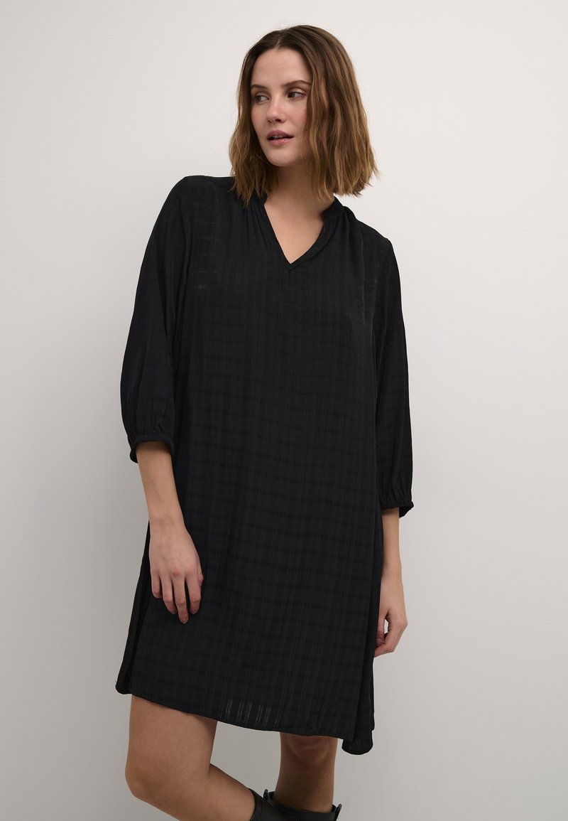 Robe noire à col en V avec des manches trois-quarts, présentant un motif en grille texturé. Tissu doux, silhouette en A et ourlet à hauteur des genoux.