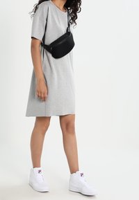 Robe grise à manches courtes, coupe décontractée, associée à un sac ceinture texturé noir et des baskets montantes blanches avec des accents de logo.