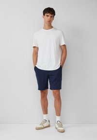 T-shirt en coton blanc associé à un short marine, avec des poches. Des chaussures comprennent des baskets beiges avec des accents blancs et marins.