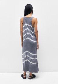 Šedé tie-dye maxi šaty s bezramenním designem a střihem na závodní záda. Tkanina má měkkou strukturu s bílými vlnitými vzory. Nosené s černými sandály.