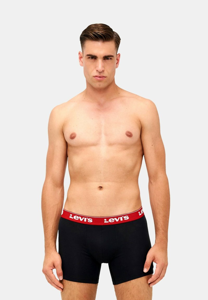 Czarne bokserki męskie z czerwoną gumką na pasku Levi's, charakteryzujące się dopasowaniem i gładkim materiałem. Model stoi na neutralnym tle.
