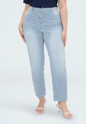 Woman wearing blue and white vertical striped pants with front buttons and white strappy heeled sandals.
