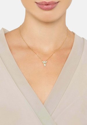 Gold necklace with a teddy bear pendant, featuring a textured surface and small embellishments, worn against a light-colored top.