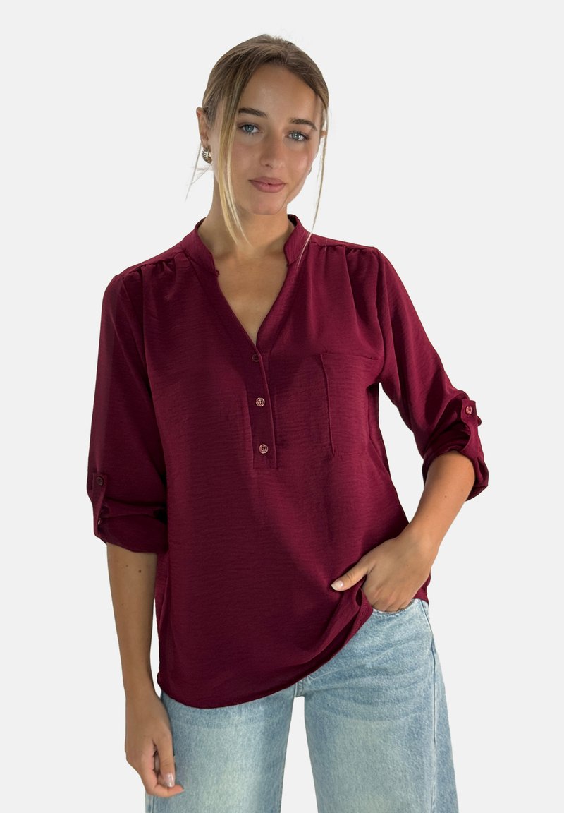 Blusa bordeaux con una placca a metà bottoni, maniche lunghe arrotolate a tre quarti e una tasca frontale, realizzata in tessuto testurizzato.