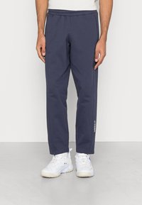 Mörkblå träningbyxor i mjukt tyg, med elastisk midja, sidofickor och en vit logodetalj på vänster ben.