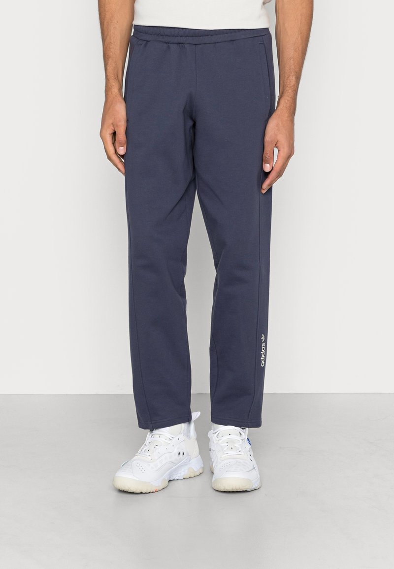 Mörkblå träningbyxor i mjukt tyg, med elastisk midja, sidofickor och en vit logodetalj på vänster ben.