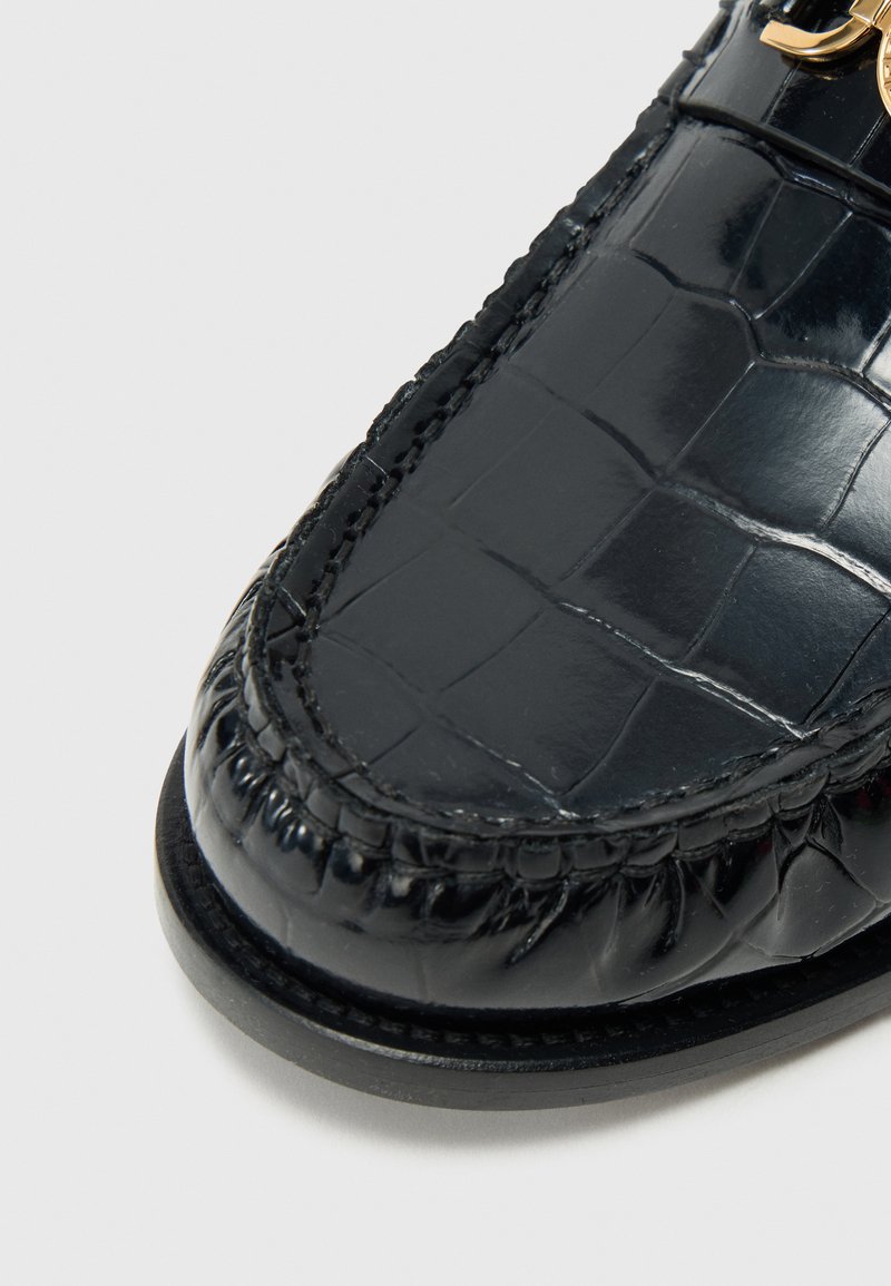 Sorte læder loafers med en blank krokodilletekstur, der har en rund tå og dekorative accenter i guld.