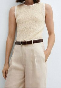 Beżowy top na ramiączkach z teksturowanym wzorem i kremowymi wykończeniami, zestawiony z beżowymi lnianymi spodniami z wysokim stanem i ciemnobrązowym skórzanym paskiem.