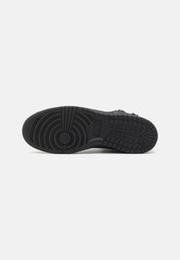 Suela de zapatilla negra con una superficie de goma texturizada. Presenta un patrón circular en el centro y líneas para tracción en toda su extensión.