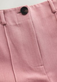 Pantaloni roz pal, croiți, dintr-un material texturat, cu pliuri clare și un detaliu cu nasture negru la talie.