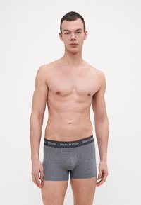 Boxer in cotone grigio con elastico nero etichettato "Marc O'Polo." Texture liscia e design aderente, indossati da un modello.