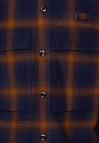 Flanellskjorta med rutmönster i blått och orange. Har svarta knappar, två bröstfickor och ett mjukt texturerat tyg.