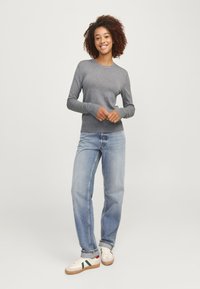 Graues Langarmoberteil mit gerippter Textur und enganliegenden Bündchen, kombiniert mit hellblauen, hochtaillierten Jeans und weißen Sneakers mit grünen und roten Akzenten.