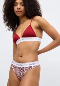 Červená rebrovaná trojuholníková podprsenka s tenkými ramienkami, v páre s bielymi a červenými vzorovanými nohavičkami, ktoré majú pás s logom Calvin Klein.