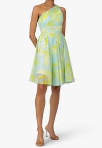 Une robe asymétrique bleu clair avec un motif de feuilles jaunes, présentant un corsage ajusté et une jupe fluide. Tissu lisse et léger.