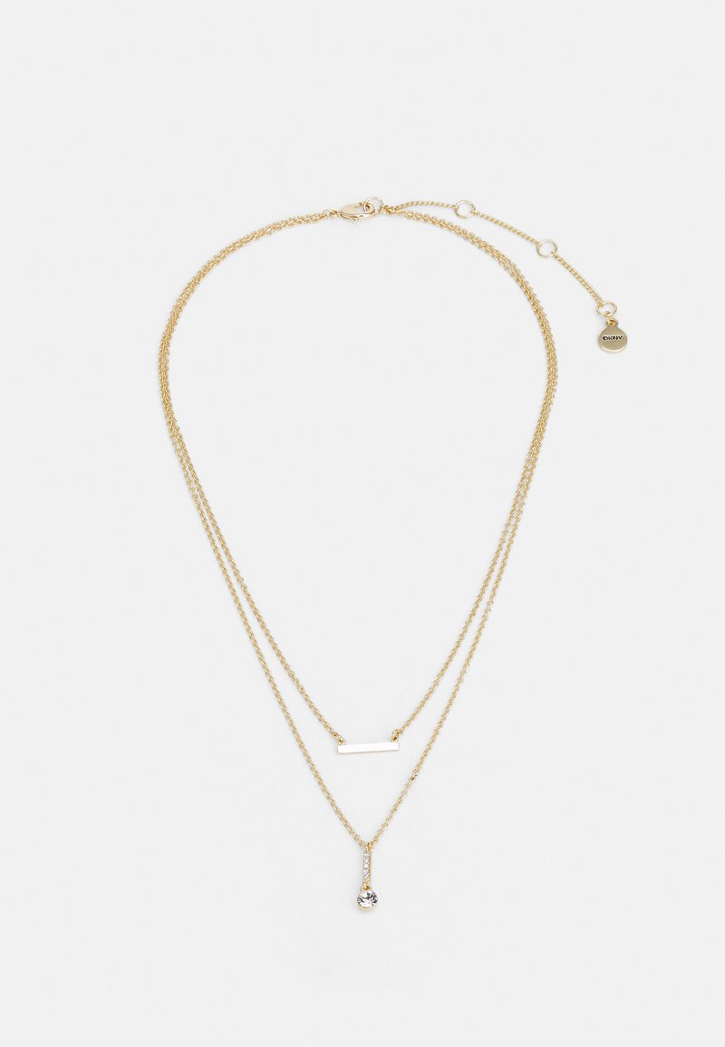 Zelta pārklājuma kaklarota ar divām ķēdes virkni. Vienai virknē ir taisnstūra stienis; otra satur piekariņu ar caurspīdīgu kristāla akcentu.