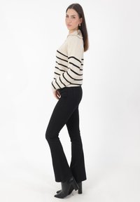 Strickpullover in Creme mit schwarzen Streifen, rundem Kragen und gerippten Bündchen. Kombiniert mit schwarzen, weit geschnittenen Jeans und hochhackigen Stiefeletten.