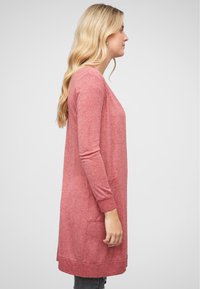 Long cardigan rose en maille douce et texturée, doté de manches longues, de poches latérales et d'un ourlet arrondi.