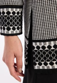 Zwart-wit gestreepte stof met houndstooth en geometrische ontwerpen. Heeft een textuurafwerking en een slanke silhouet.