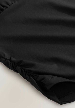 Nahaufnahme eines schwarzen Stoffs mit gesammelter elastischer Naht am Rand, die Textur und Naht zeigt.