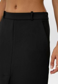 Schwarze maßgeschneiderte Hosen verfügen über einen glatten Stoff, einen strukturierten Bund mit Gürtelschlaufen und Seitentaschen und zeigen ein elegantes Design.