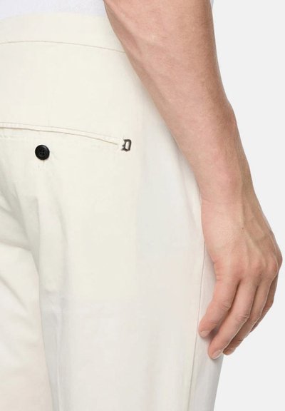 Pantaloni beige chiaro con una texture liscia, dotati di una tasca posteriore con un bottone nero e un'accenno cucito visibile vicino alla tasca.