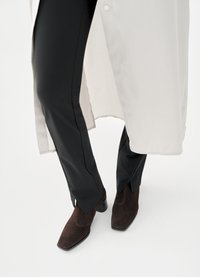 Καφέ μποτάκια από σουέντ με τετράγωνη μύτη, σε συνδυασμό με μαύρο στενό παντελόνι και μακριά, ανοιχτόχρωμη πουκαμίσα.