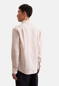 Camicetta a righe beige a maniche lunghe con texture sottile, colletto a risvolto e polsini con bottoni. Vestibilità aderente con orlo leggermente curvato.