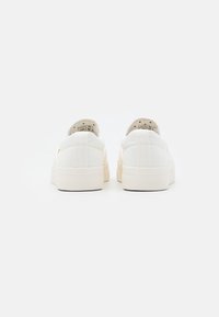 Ein Paar weiße Leinensneaker mit dicken Gummi-Sohlen, von hinten auf einem schlichten weißen Hintergrund gezeigt.