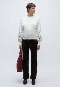 Λευκό φούτερ με πολύχρωμη κεντημένη λουλουδένια διακόσμηση στα μανίκια φουσκωτού στυλ, συνδυασμένο με μαύρο καμπάνα παντελόνι και κόκκινη τσάντα ώμου.