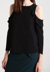 Černý top s odhalenými rameny a volány, dlouhé rukávy a hladký materiál; má pohodlný střih a jednoduchý výstřih.