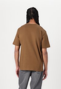 Brun bomulds t-shirt med korte ærmer og rund halsudskæring, der har en afslappet pasform. Bagfra ses en glat tekstur og et enkelt design.