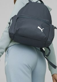 Mochila de color azul marino oscuro con un acabado texturizado, que cuenta con un bolsillo frontal con cremallera y el logo blanco de Puma. Correas ajustables para un uso cómodo.